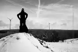 'Rodler auf einem schneebedecktem Hügel vor einer Gruppe von Windrädern' in a higher resolution